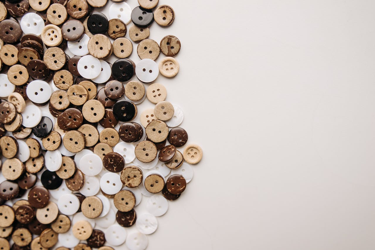 Assorted vintage buttons, arranged on a white surface, featuring various shades of brown, tan, black, and white, made from materials like glass and plastic, with two and four-hole designs