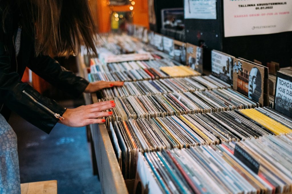 Person browsing vinyl records in a store, organized rows of albums, music posters in background, hands flipping through covers