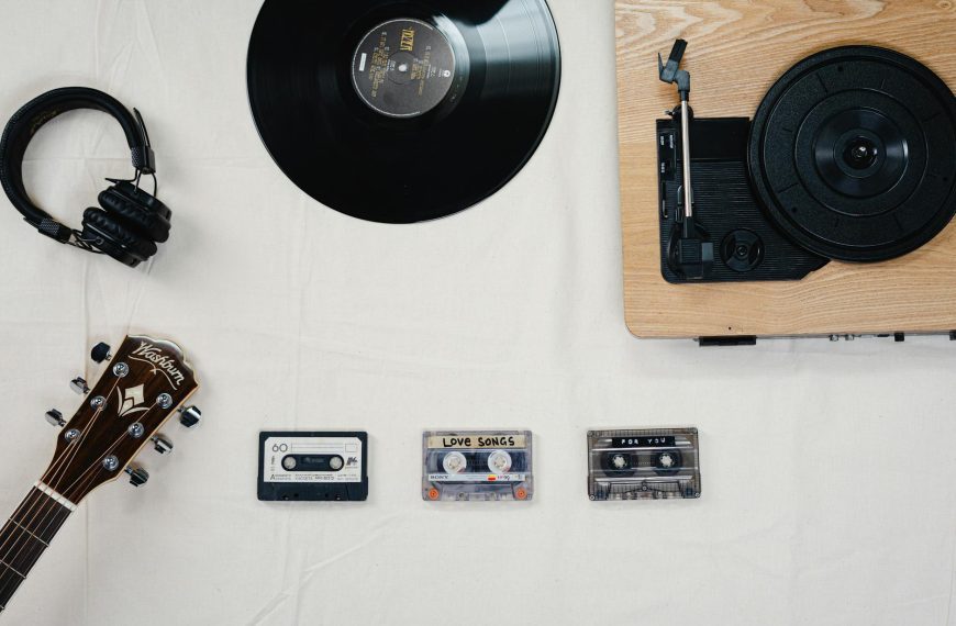 Flat lay of guitar, vinyl, cassettes, and headphones showcasing a classic music collection.
