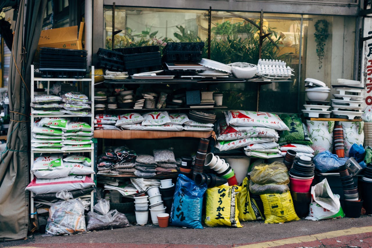 Outdoor display of stacked fertilizer bags, gardening pots, and supplies outside a plant shop