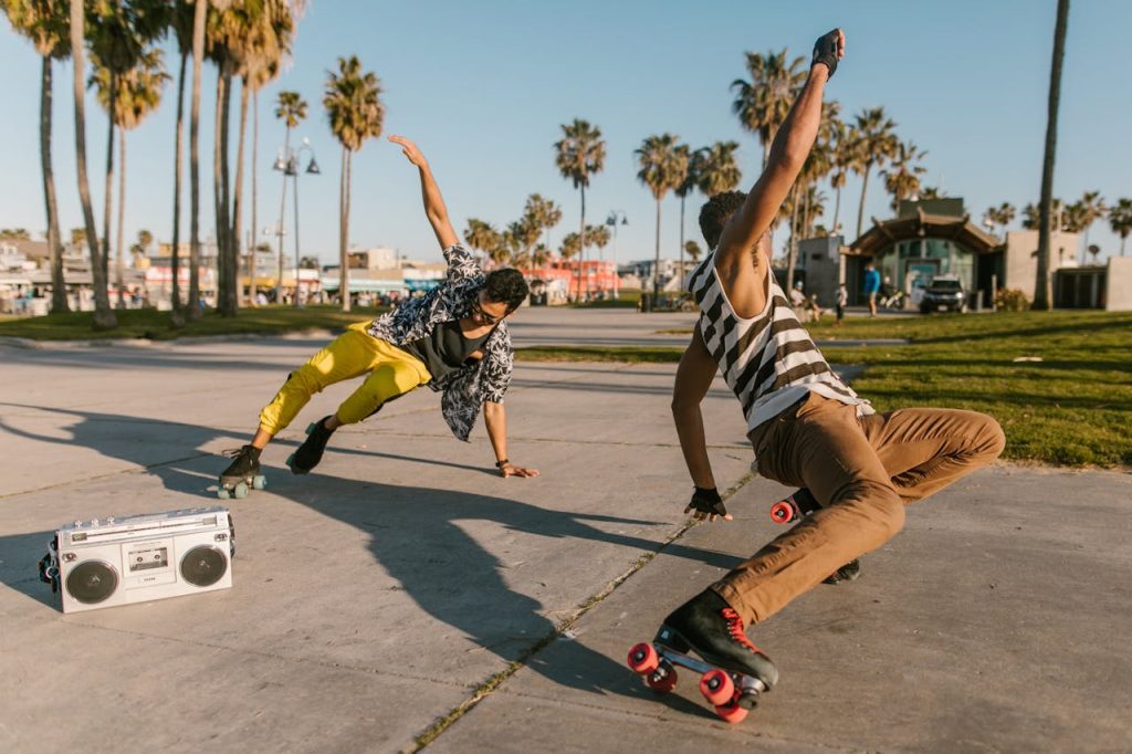 two men roller skating on a sunny day, performing dance moves, vintage boombox on ground, palm trees, beach park setting