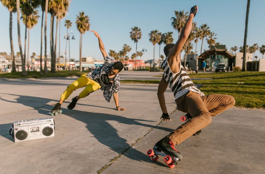 two men roller skating on a sunny day, performing dance moves, vintage boombox on ground, palm trees, beach park setting