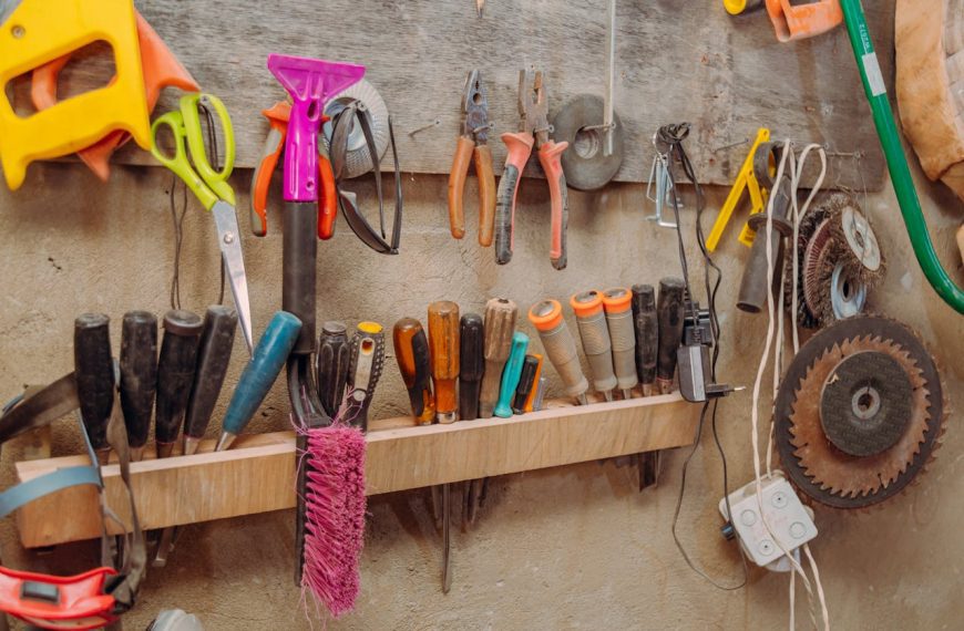 Assorted hand tools hanging on a wall-mounted rack, screwdrivers, pliers, scissors, brushes, electric cords, saw blades