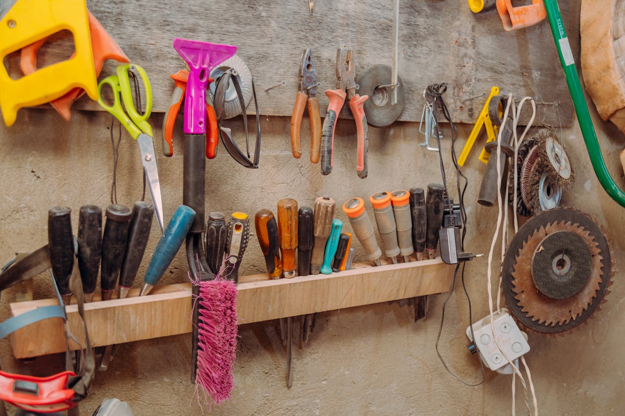 Assorted hand tools hanging on a wall-mounted rack, screwdrivers, pliers, scissors, brushes, electric cords, saw blades