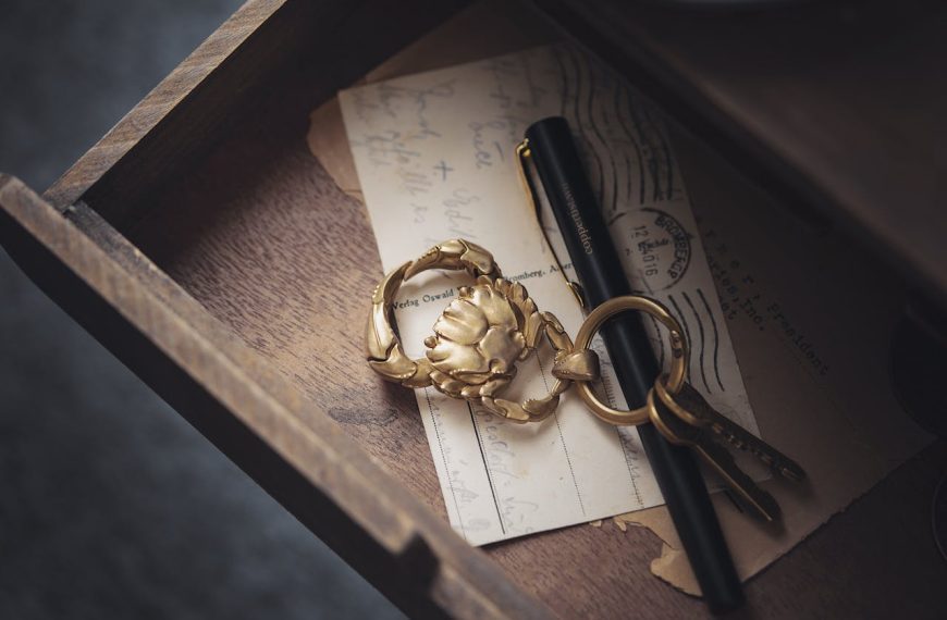 open wooden drawer with vintage keys, gold keychain, black fountain pen, and old handwritten postcards inside