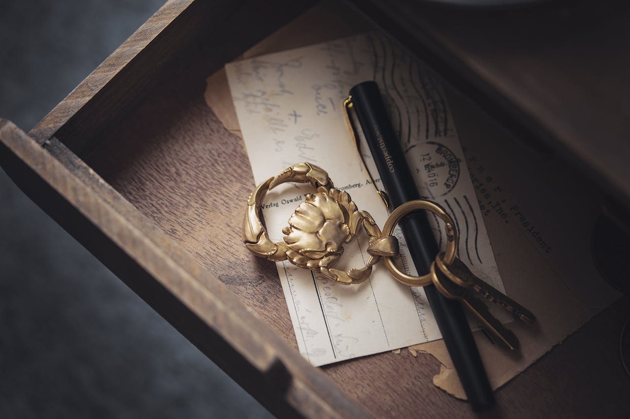 open wooden drawer with vintage keys, gold keychain, black fountain pen, and old handwritten postcards inside