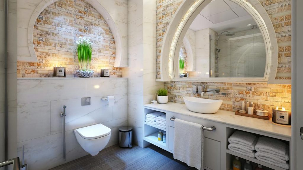 Modern bathroom with arched stone wall accents, wall-mounted toilet, vessel sink on white vanity, large mirror, decorative lighting, indoor plant on shelf