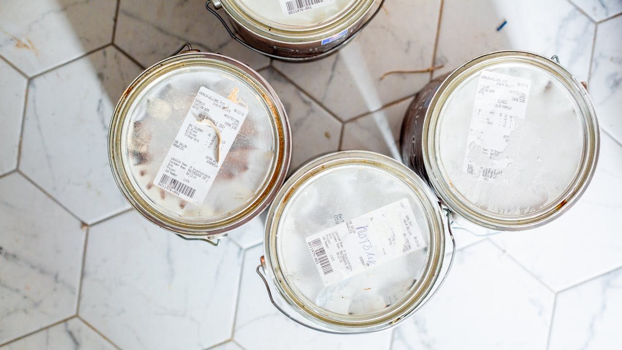 Top view of four sealed paint cans with labels, placed on a white hexagon-tiled floor