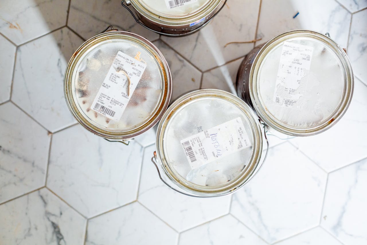 Top view of four sealed paint cans with labels, placed on a white hexagon-tiled floor