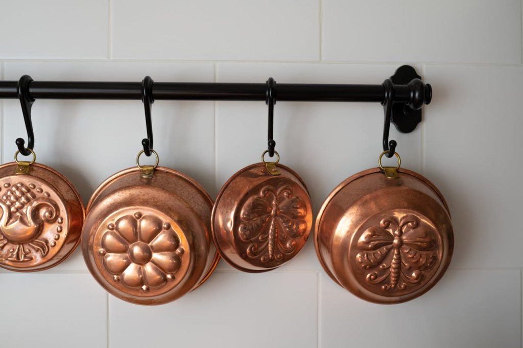 Copper molds hanging on black metal hooks, four decorative vintage-style molds, mounted on a white kitchen wall, evenly spaced and neatly arranged