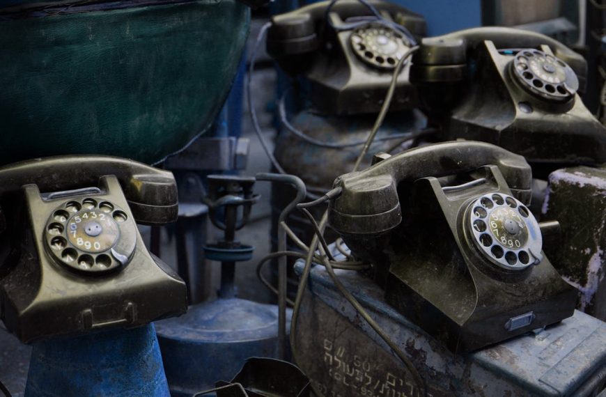 Collection of vintage rotary telephones with circular dials stacked together, showing worn black cases and coiled cords