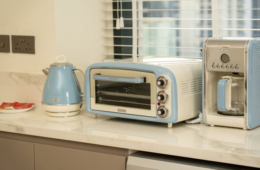 Aesthetic kitchen counter with pastel blue kettle, toaster oven, and coffee maker beside a window with white blinds