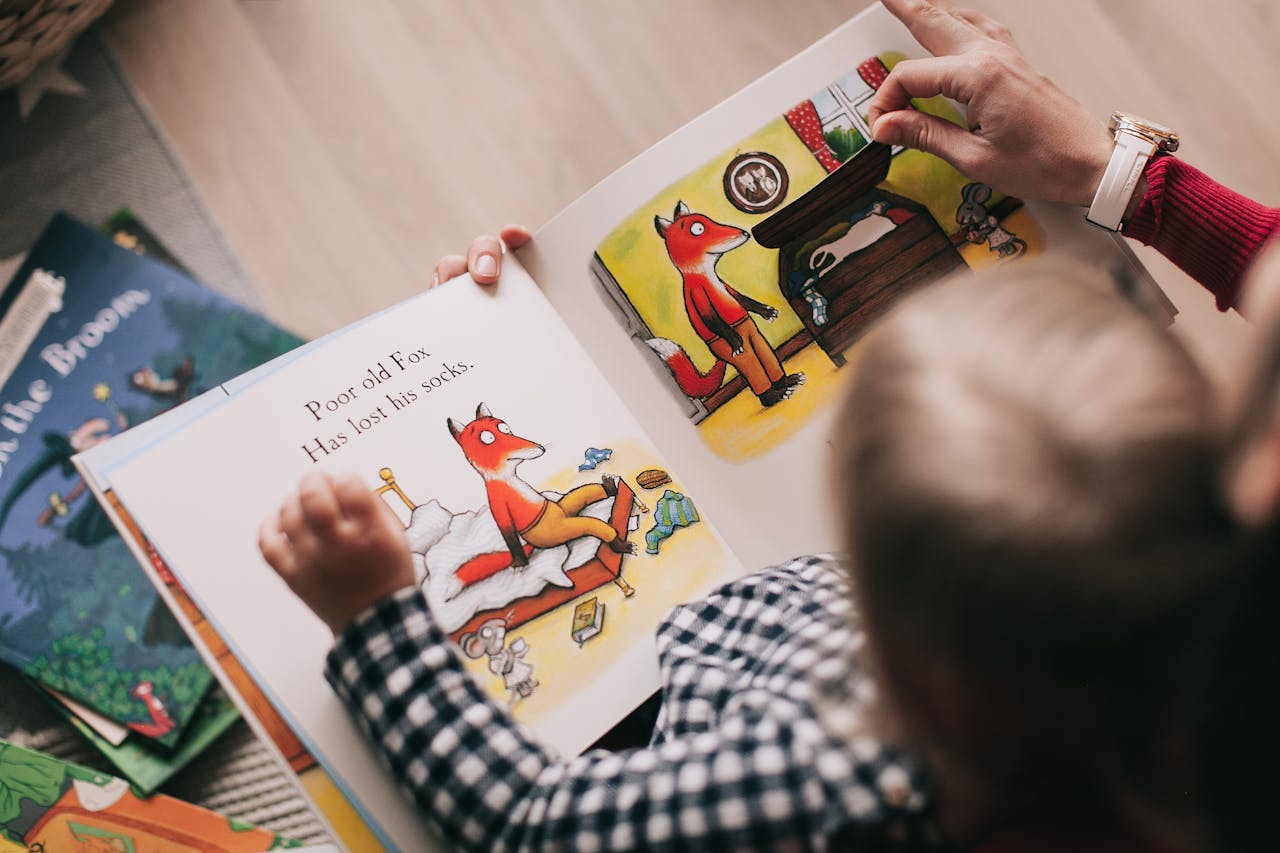 Adult with red sleeve and watch reading fox-themed children's book to child in checkered shirt, page shows "Poor old Fox"
