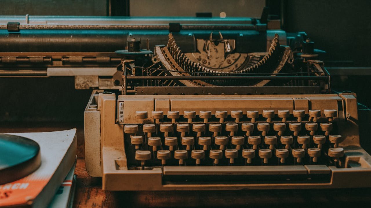 Vintage mechanical typewriter with beige keys on wooden desk, displaying its internal mechanisms and roller, with books nearby