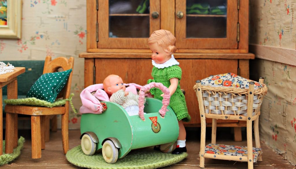 Vintage-style dolls in a miniature room, with a green stroller, wooden furniture, and colorful details creating a cozy scene