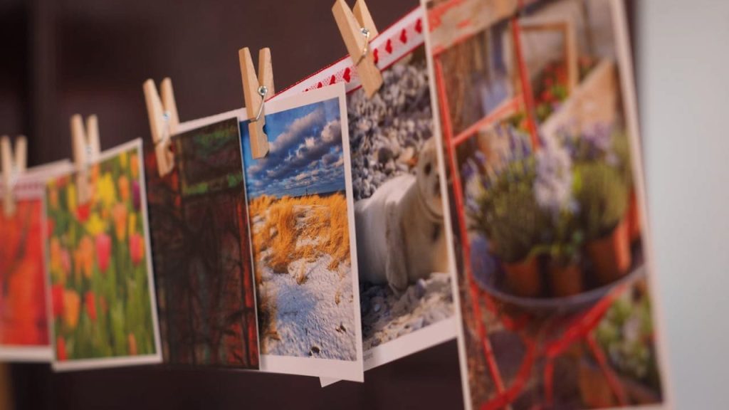 Colorful photographs hanging on a string with wooden clothespins, showcasing nature scenes and flowers, in a soft indoor setting