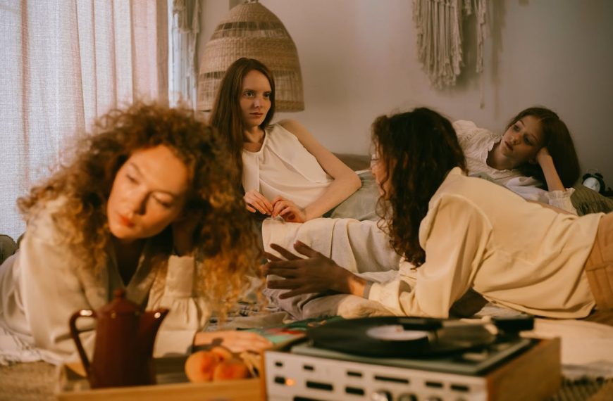 three women in soft lighting sitting indoors, one leaning forward, one listening, vinyl record player, cozy room setup