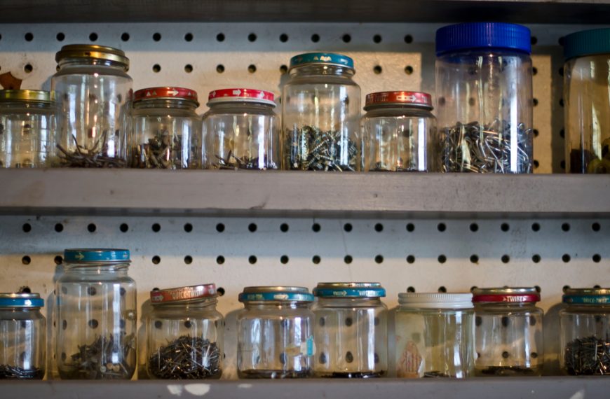 Glass jars filled with assorted screws and nails, metal shelving unit, pegboard backdrop, organized workshop storage
