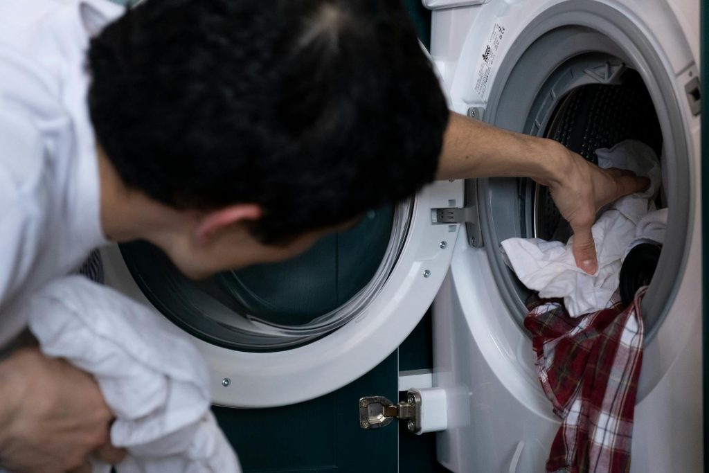 A person loading or unloading laundry from a front-loading washing machine, placing a mix of white and red clothing items inside