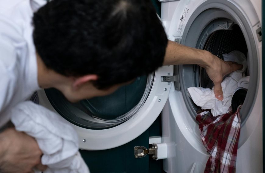 A person loading or unloading laundry from a front-loading washing machine, placing a mix of white and red clothing items inside