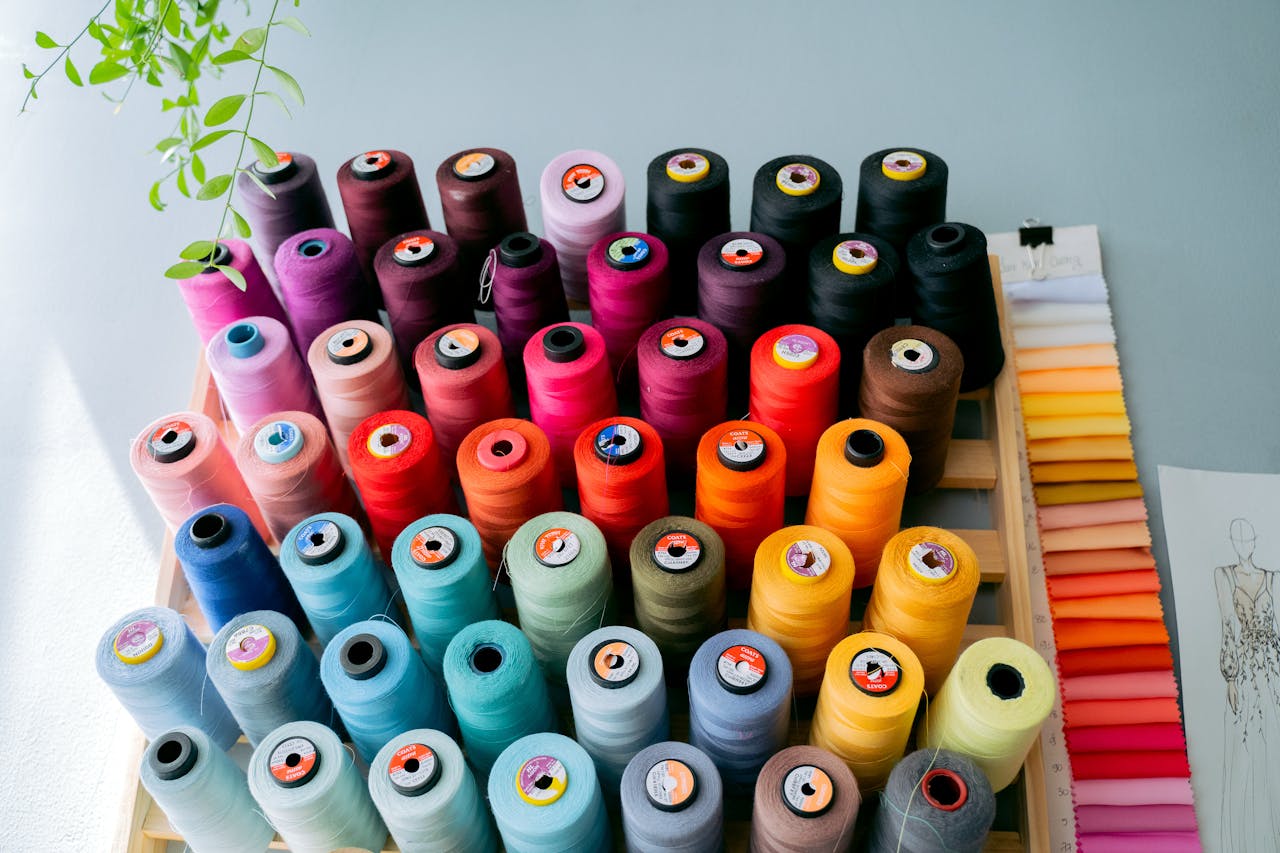 Colorful thread spools neatly arranged on a wooden rack, wide range of hues from pastels to bold tones, sewing or fashion design workspace