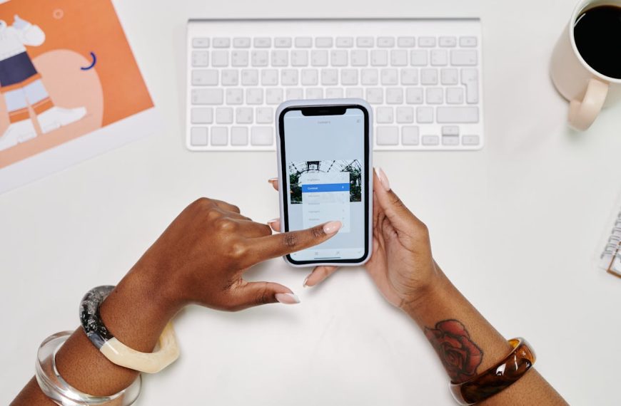 Person adjusting contrast settings on smartphone, white keyboard in background, coffee mug on desk, graphic print and notepad nearby