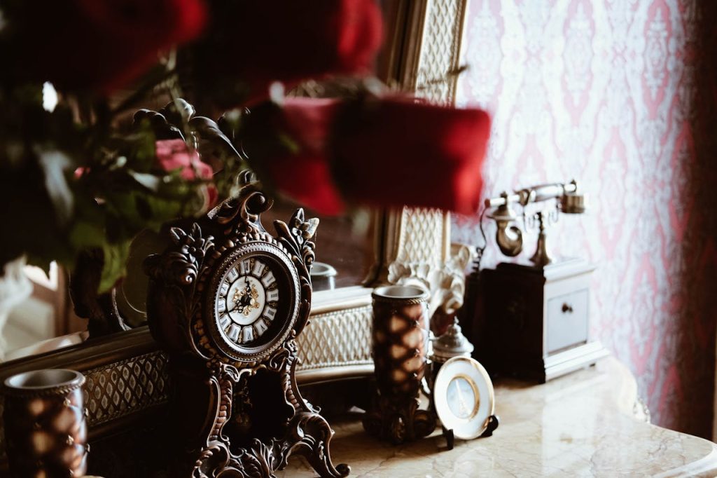 Vintage ornate clock on marble vanity, antique rotary telephone, decorative mirror, roses in foreground, classic wallpaper backdrop