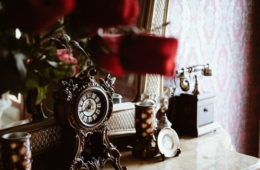 Vintage ornate clock on marble vanity, antique rotary telephone, decorative mirror, roses in foreground, classic wallpaper backdrop