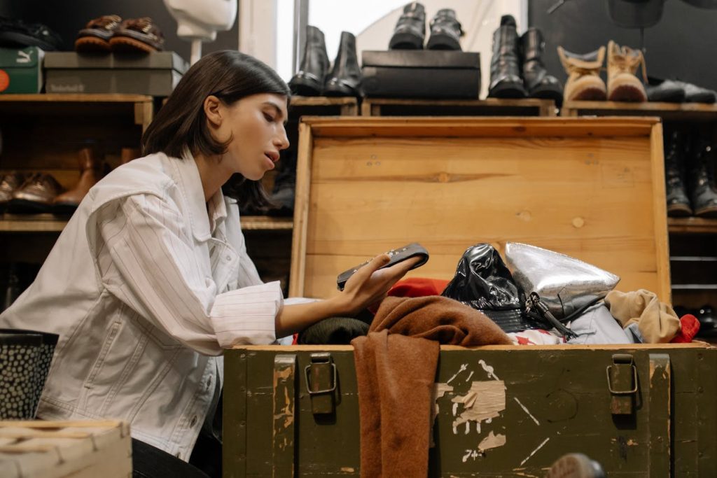 Woman looking through vintage clothes in a wooden chest, thrift store setting, shoes in the background, secondhand fashion