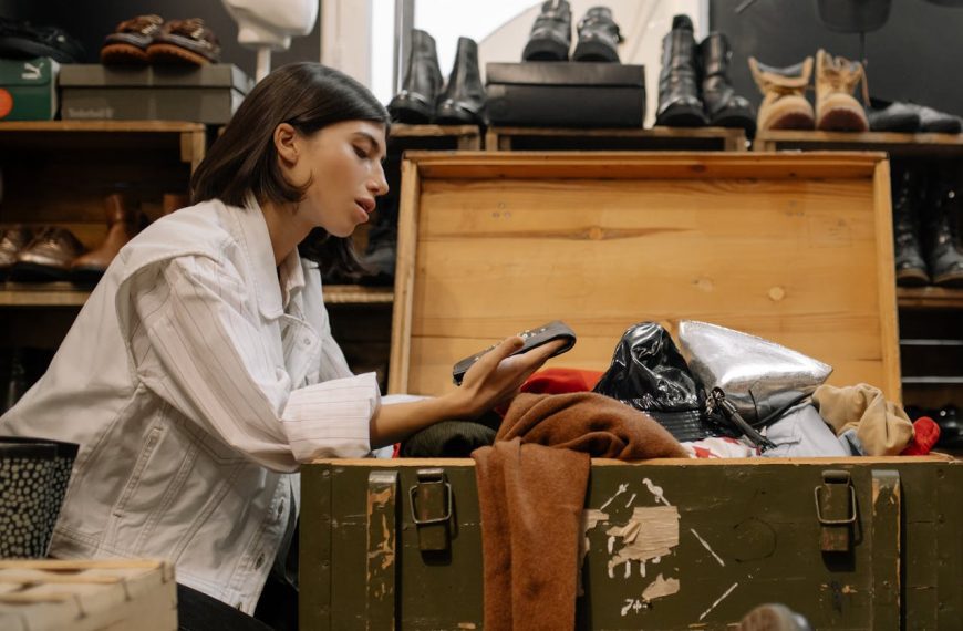 Woman looking through vintage clothes in a wooden chest, thrift store setting, shoes in the background, secondhand fashion