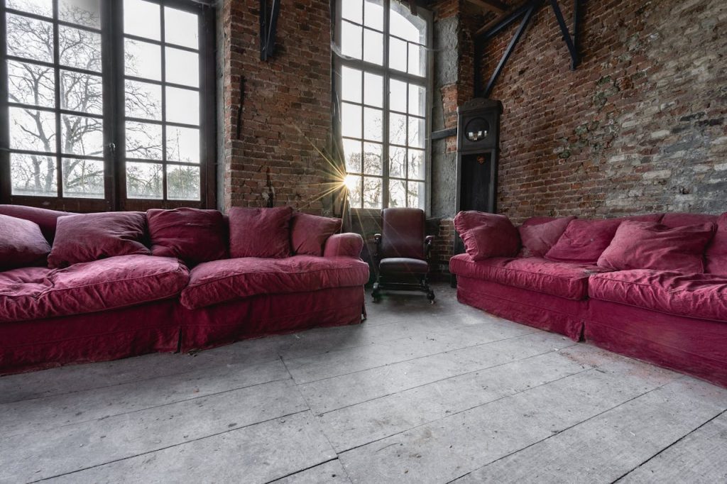vintage room with exposed brick walls, deep red velvet sofas, wooden floor with a weathered look, rustic and cozy atmosphere