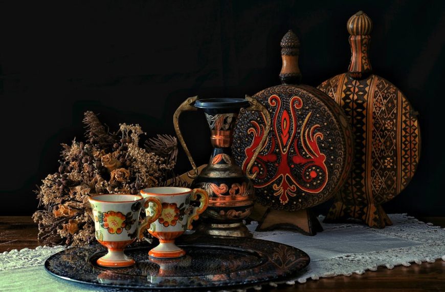 Vintage ceramic tea cups with floral patterns, ornate metal pitcher, round wooden trays with ethnic designs, dried flowers, lace table runner
