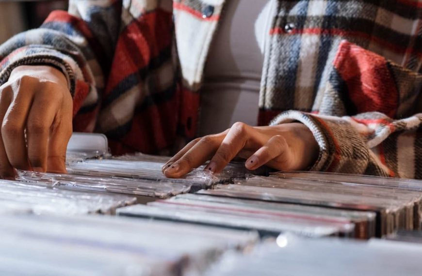 Person wearing a plaid jacket flipping through rows of CD cases in a music store