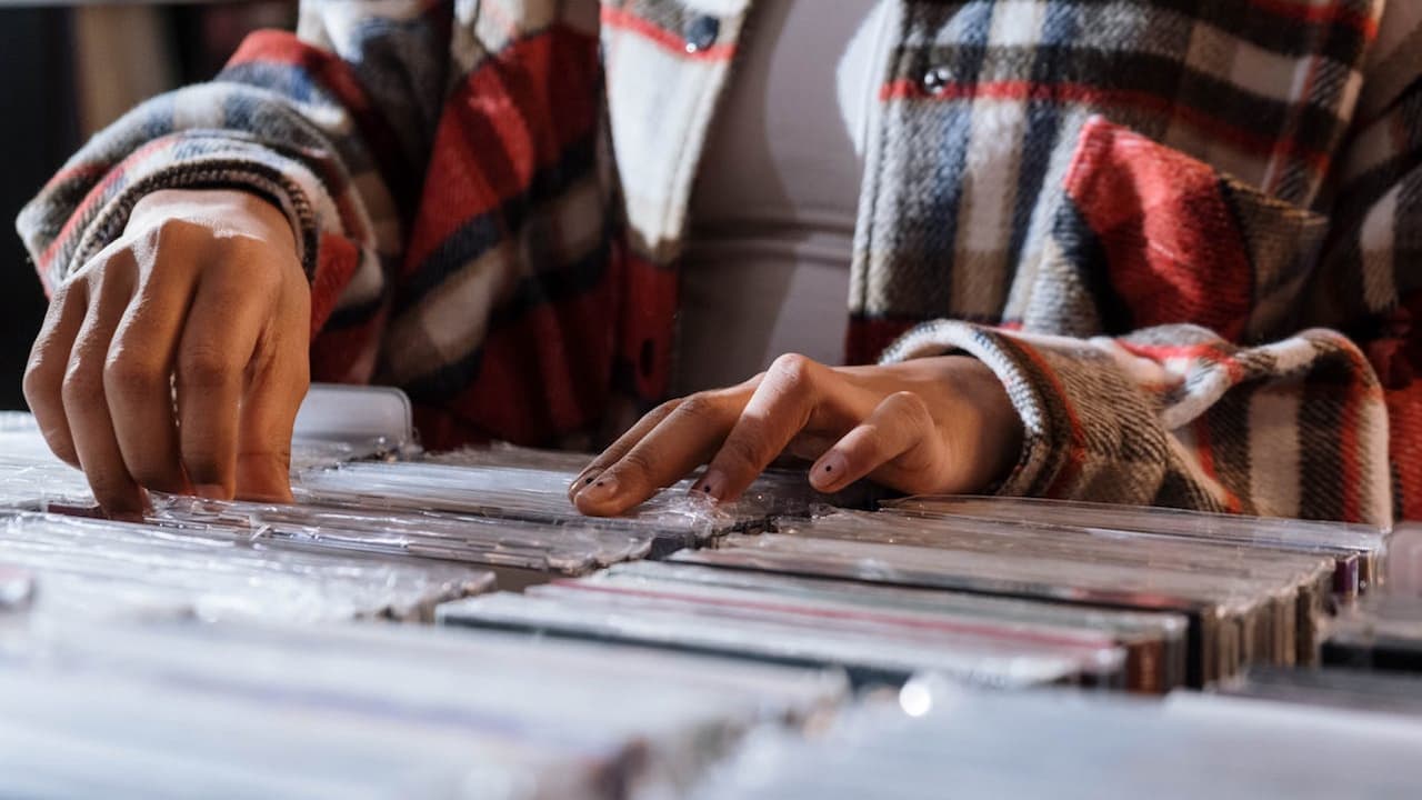 Person wearing a plaid jacket flipping through rows of CD cases in a music store