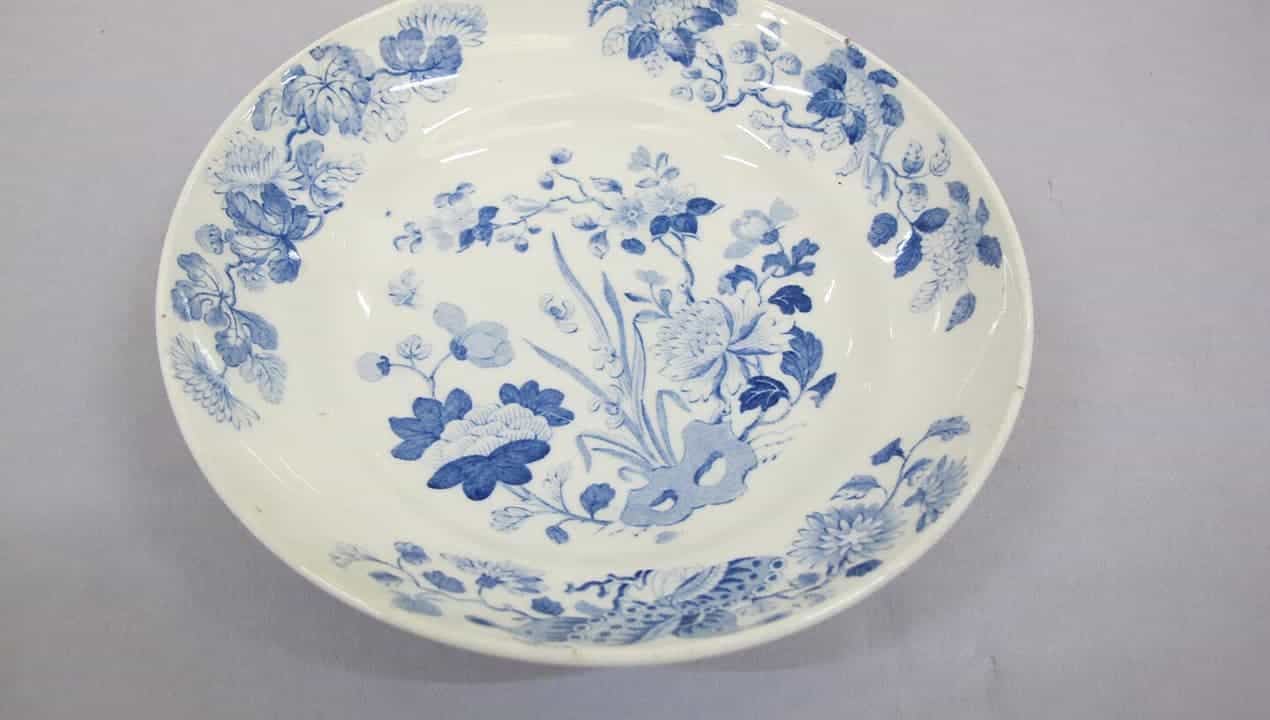 White ceramic plate, decorated with delicate blue floral patterns, classic design, shallow bowl shape, placed on a light gray surface