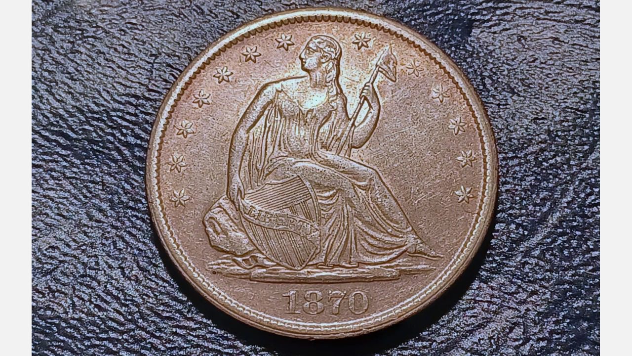 1870 Seated Liberty silver dollar coin showing Lady Liberty holding a shield and staff, surrounded by 13 stars, placed on a dark textured surface