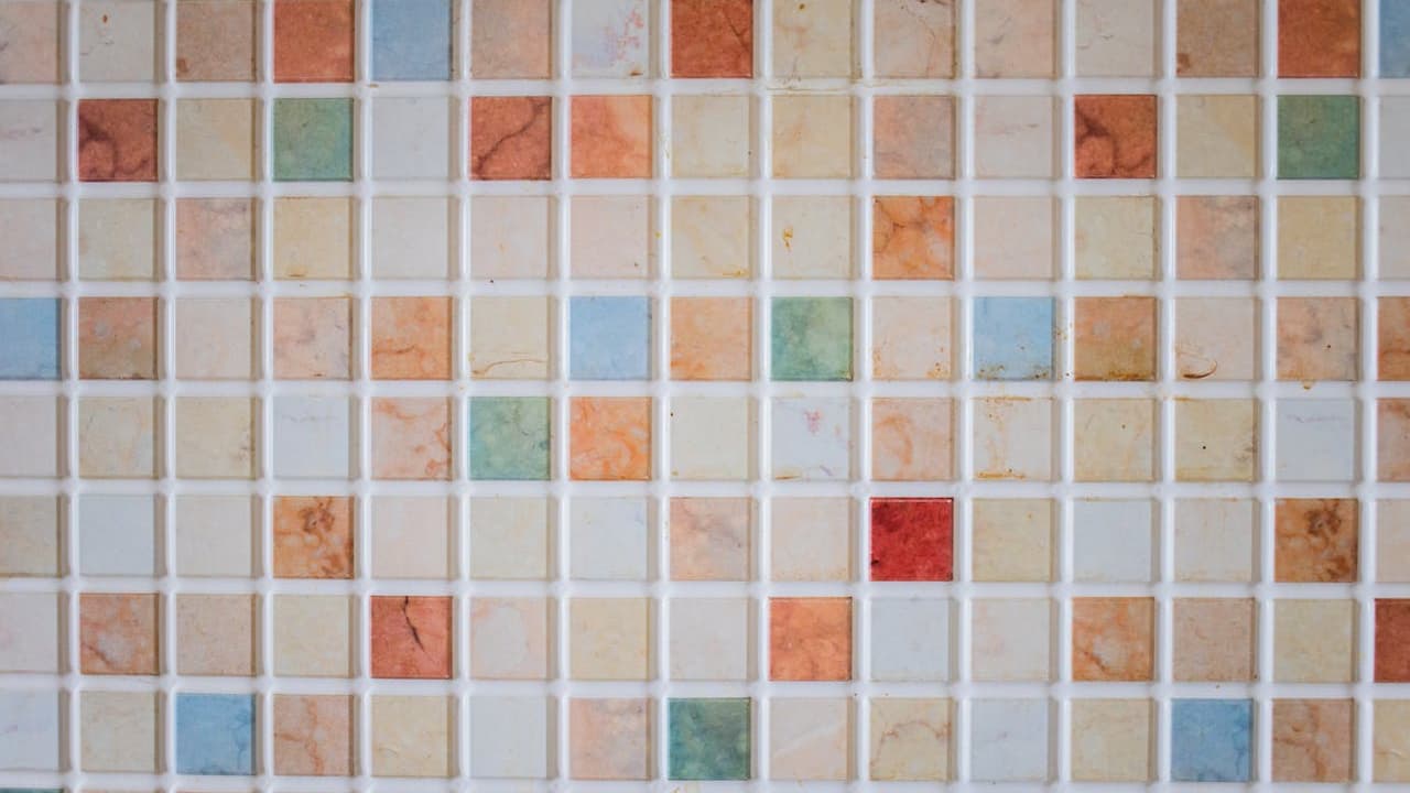 Colorful mosaic tile wall, small square tiles, arranged in a grid pattern, various colors including red, orange, blue, green, beige, and white, glossy finish, slight marbling texture, clean grout lines, symmetrical layout