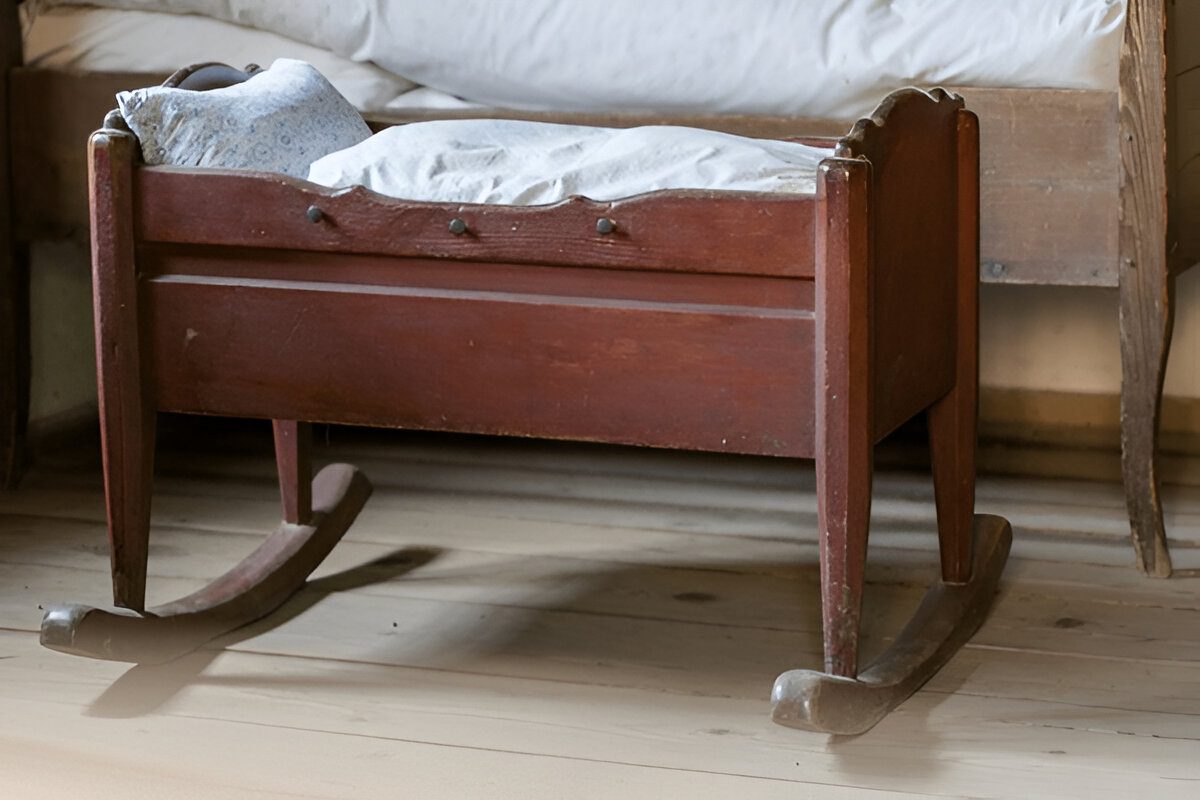 Wooden baby cradle, curved rockers at the base, white cushioned bedding, placed on a light wooden floor, vintage or antique design