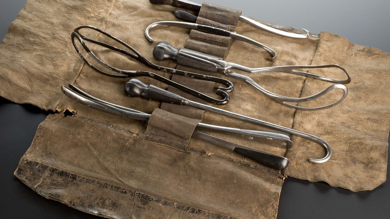 Set of antique surgical tools with black and polished metal handles, laid out on a worn leather roll