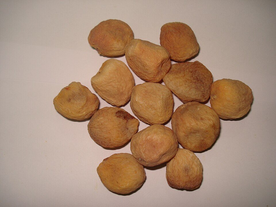 Dried apricot kernels, arranged in a cluster, light brown color, rough texture, placed on a plain white background