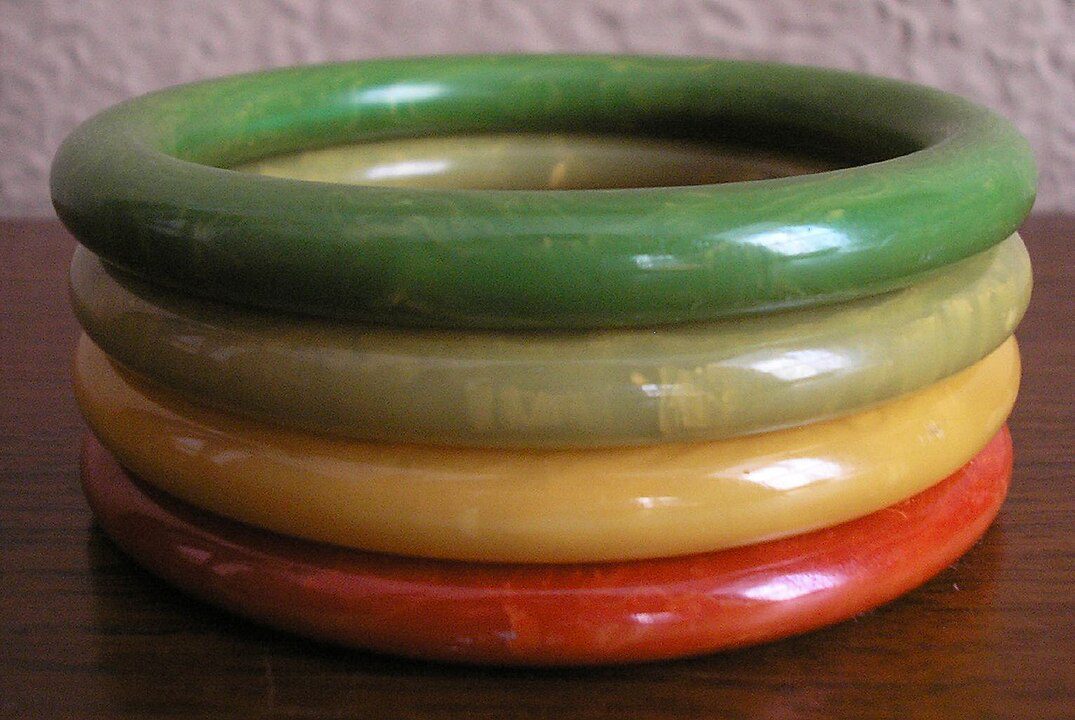 Stack of four colorful plastic bangles, arranged in green, olive, yellow, and red order, placed on a wooden surface