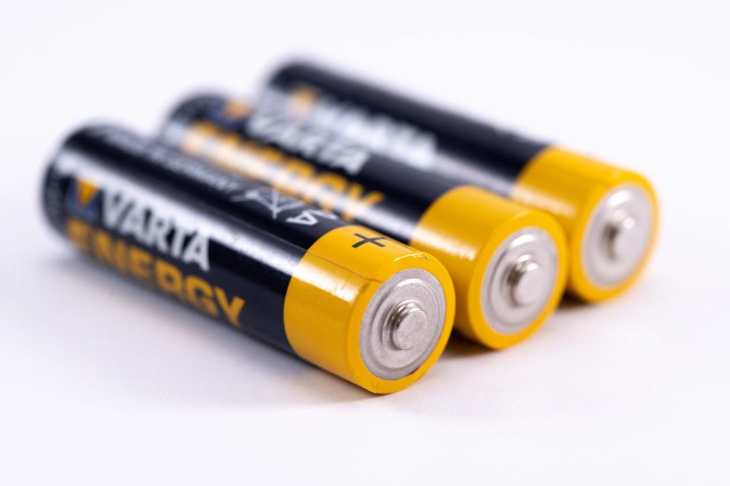Three AA batteries, black and yellow casing, arranged in a row, silver terminals facing forward, white background