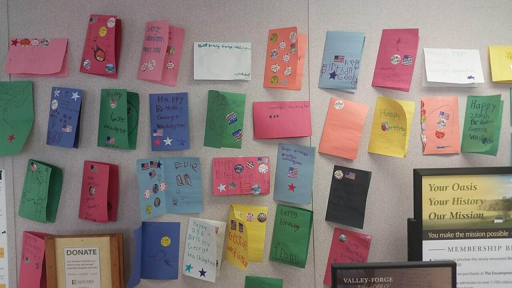 Colorful handmade cards displayed on a wall, arranged in neat rows, decorated with stickers, drawings, and handwritten messages