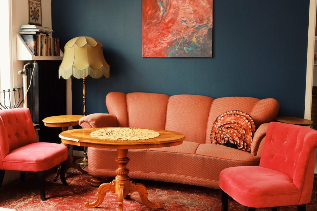 Vintage living room, orange sofa and chairs, wooden coffee table, dark blue wall, abstract red artwork, antique floor lamp, cozy and retro interior design