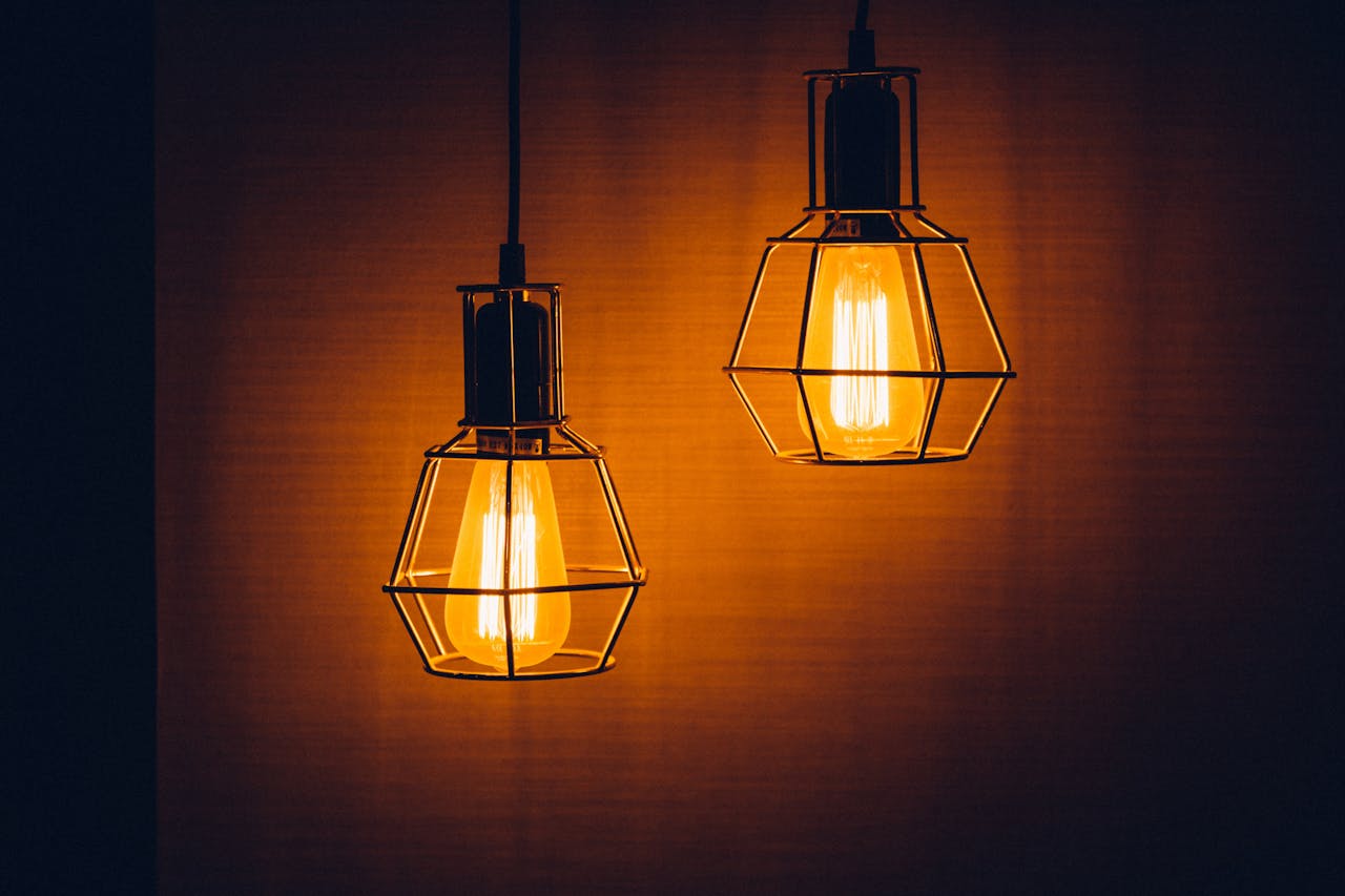 Two vintage-style hanging light bulbs, enclosed in wire cages, glowing warmly against a dark, amber-toned background