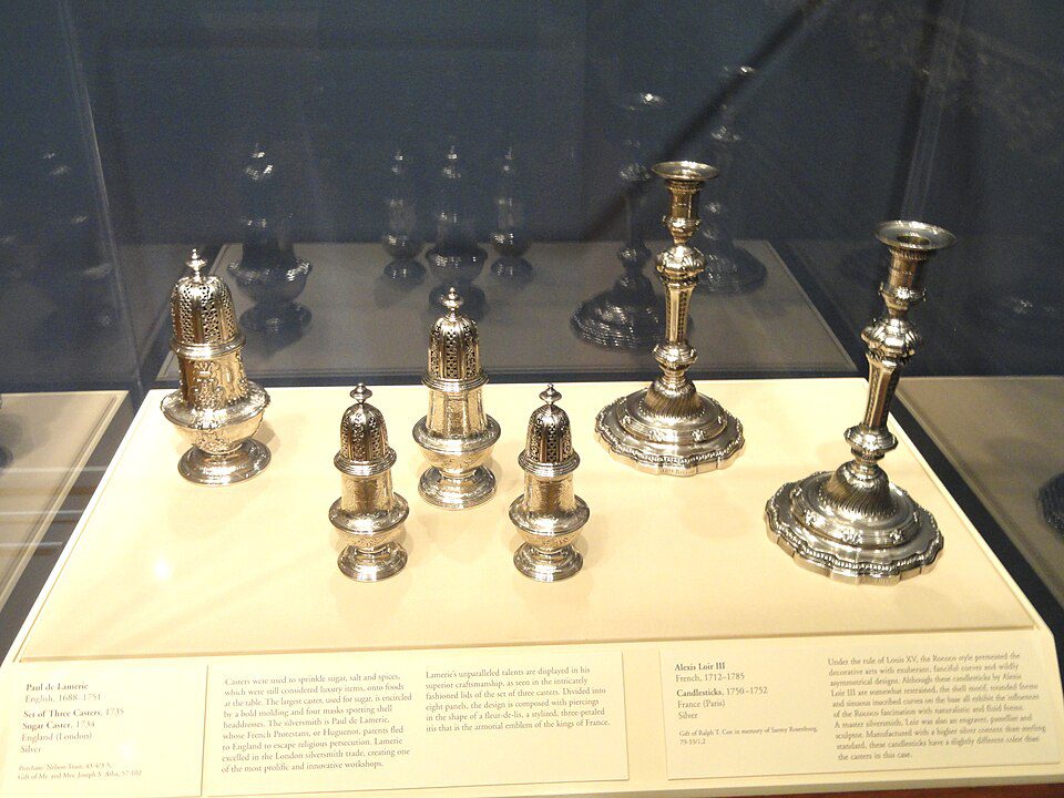 Silver ceremonial candlesticks, displayed on a museum exhibit platform, placed in a glass case, arranged in ascending height order