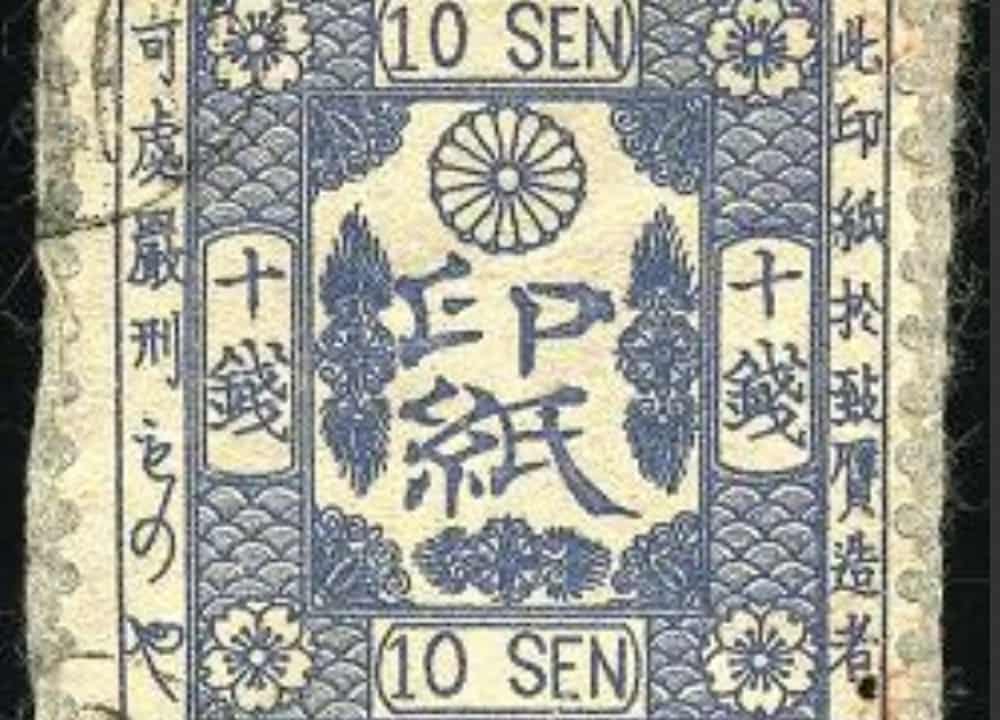 Vintage Japanese revenue stamp, 10 sen denomination, printed in blue with floral emblems, chrysanthemum crest at the top center, Japanese characters in bold at the center, bordered by intricate traditional patterns and vertical kanji script along the sides
