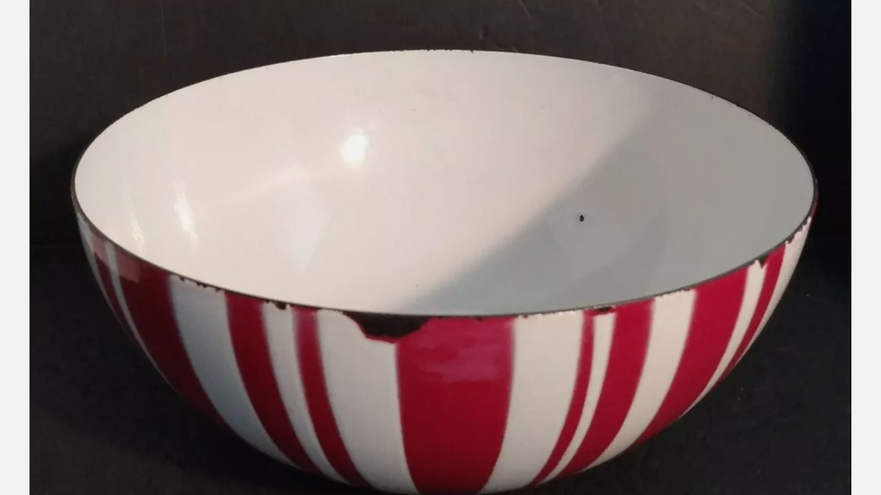 Vintage enamelware bowl with red and white vertical stripes, slightly chipped along the rim, placed against a dark background