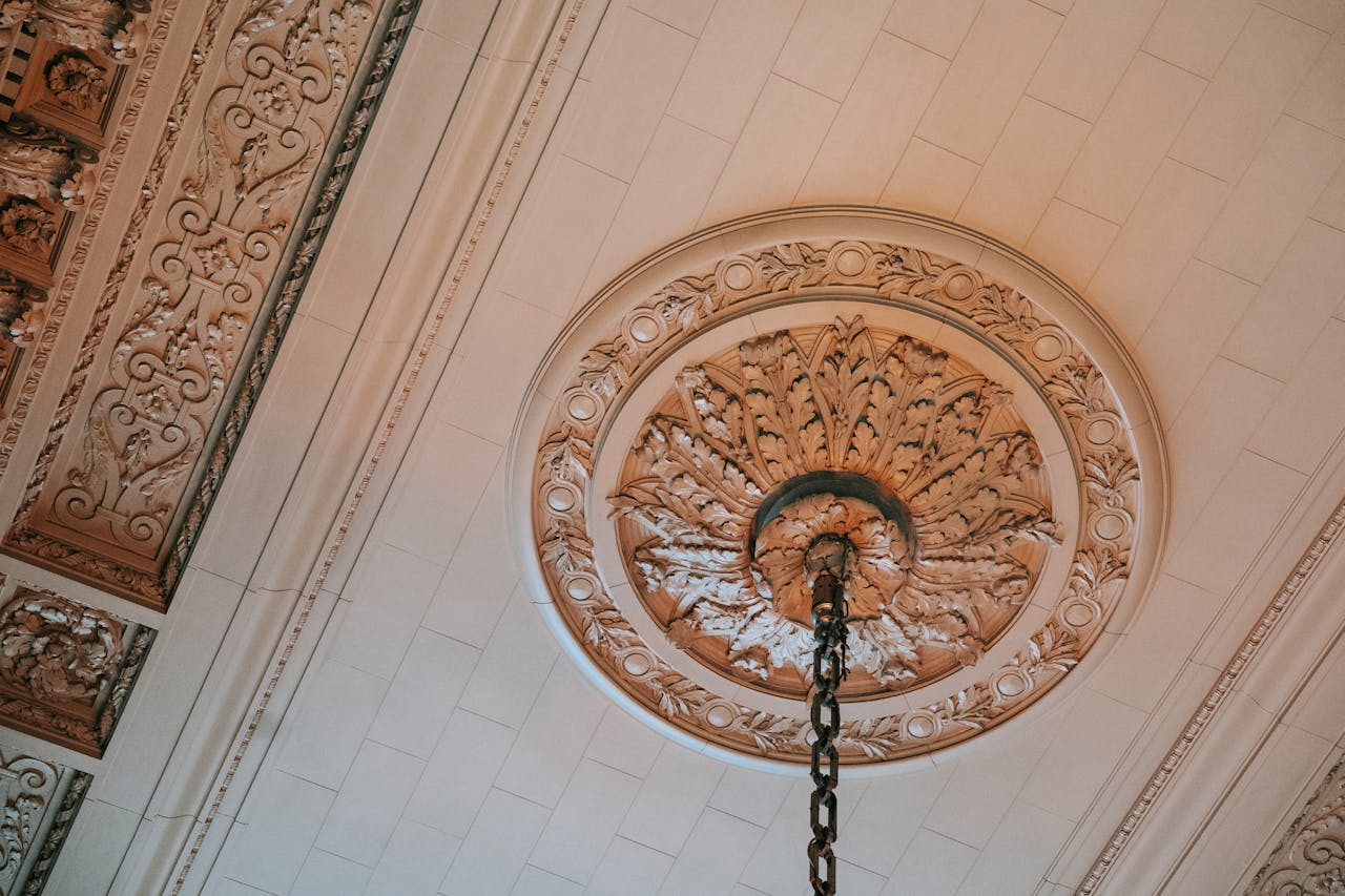 Ornate ceiling medallion, circular decorative molding, antique plaster design, attached to hanging light fixture, classical architecture style, elegant interior detail, white and beige color scheme, vintage ceiling decor