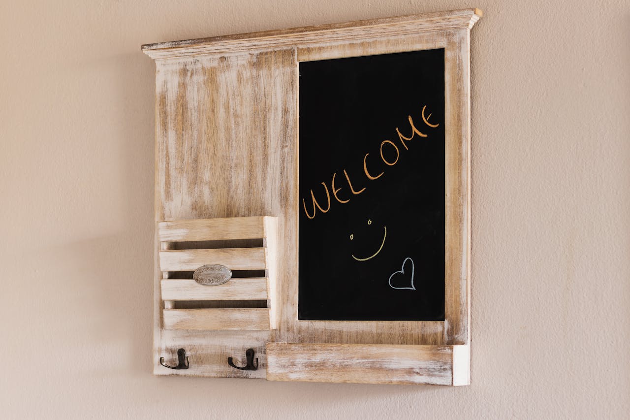 Rustic wooden wall organizer with a black chalkboard panel displaying the word "WELCOME" in orange with a smiley face and heart doodle